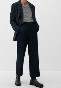 Mörkblå, löst sittande byxor ihop med en kort svartvit randig topp och en mörk kavaj; svarta ankelboots fulländar outfiten.