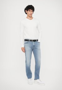 Bijela košulja dugih rukava s V-izrezom, svijetloplave traperice s izblijedjelim dijelovima, crni pojas i bijele tenisice. Jednostavna, ležerna odjeća.