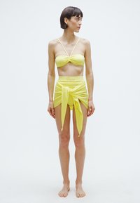 Sárga bikiniszett csavart elülső résszel ellátott felsővel és magas derekú alsóval, csomós részlettel. Simább textúra, minimalista dizájn és rugalmas anyag.