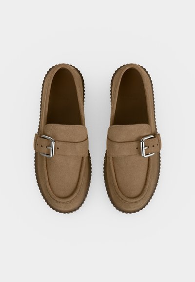 Paire de mocassins en daim marron avec boucles argentées et semelles en caoutchouc rainurées, vue de dessus sur fond blanc.