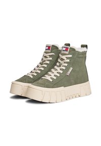 Baskets montantes en suède vert avec des semelles épaisses crème, des lacets blancs et une doublure en polaire, marquées des logos Tommy Jeans.