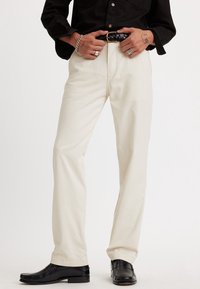 Beiga raka byxor i bomull, med gylf, bältesslingor och synlig sömnad. Kombination med svarta kostymskor.