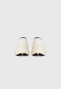 O pereche de adidași off-white cu talpă groasă crem și talon negru, prezentată din spate pe un fundal alb simplu.