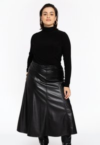 Un haut col roulé noir associé à une longue jupe en cuir noir avec une texture lisse et des détails de couture. La tenue a une taille ajustée.