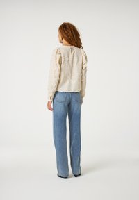 Crème bloemen-geembosste blouse met pofmouwen, keyhole-detail op de rug, gecombineerd met relaxte lichtblauwe jeans. Gelaagde stof met een zachte uitstraling.