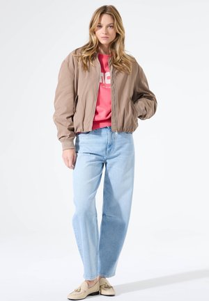 Light brown bomber jacket with a ribbed collar, paired with a pink sweatshirt and light blue wide-leg jeans, completing the casual look.