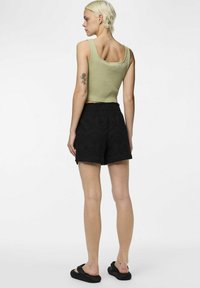 Ribbat gröncrop-top i olivgrön, tillsammans med svarta broderade shorts med scalloped nederkant. Modell som står med svarta sandaler, sedd från baksidan.