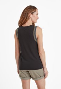 Black sleeveless tank top with decorative stitching on shoulders. Soft fabric, relaxed fit, paired with rolled hem olive green shorts.