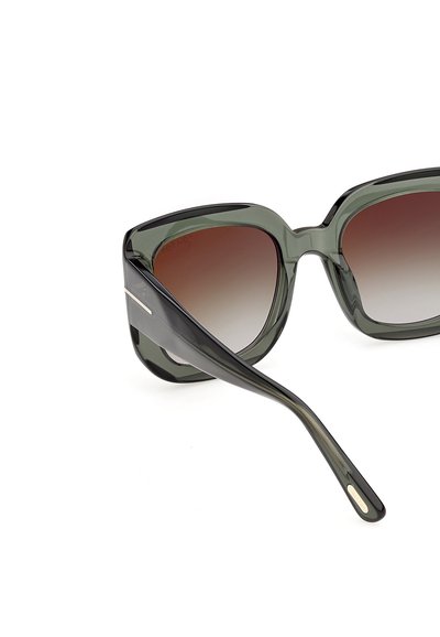 Lunettes de soleil carrées surdimensionnées avec des montures translucides vert foncé et des verres marron dégradés, vues sous un angle avant latéral.