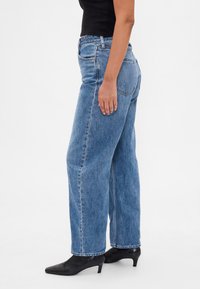 Hele sinise tooniga kõrge vöökohaga teksad sirgete säärega, valmistatud denimist. Omavad tagataskuid ja nähtavat õmblust ning kantud mustade kontsadega.