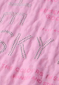 Tela rosa con tachuelas plateadas en relieve en forma de letras, con texto impreso en diferentes tonos de rosa. El diseño del texto presenta una apariencia texturizada.