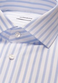 Chemise blanche à rayures verticales bleu clair, col boutonné, avec une étiquette Seidensticker à l'intérieur du col.