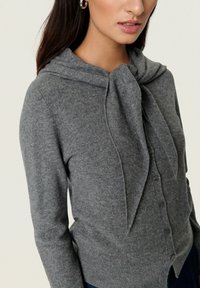 Grå cardigan med en bundet halslærred, knaplukning og ribbede manchetter. Blød strikket tekstur og tætsiddende design.
