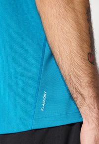 Turkusowa koszulka sportowa z teksturowanym, oddychającym materiałem. Posiada białą naszywkę "FLASHDRY" z boku, krótkie rękawy oraz dopasowany krój.