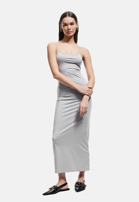 Vestido gris ajustado con tirantes finos, largo hasta los tobillos, de textura suave, combinado con planos negros de punta con acentos decorativos.