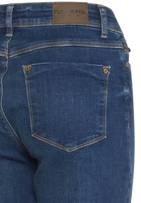 Vedere din spate a unei perechi de blugi din denim albastru închis, cu un singur buzunar în spate și o etichetă din piele maro inscripționată "Pulz Jeans" pe talie.