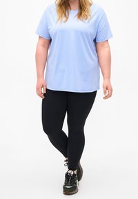 Camiseta atlética de manga corta de color azul claro combinada con leggings negros y zapatillas oscuras verdes, con tejido texturizado y un corte relajado.