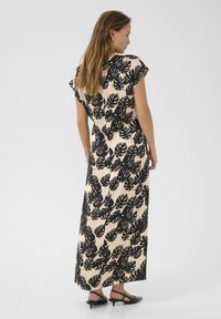 Maxiklänning i mjukt, lätt tyg med ett svart lövmönster på en beige bakgrund. Avslappnad passform, korta ärmar och knälång nederkant.