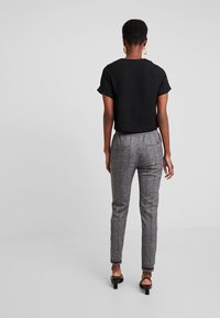 Czarna bluzka z krótkim rękawem zestawiona z szarymi spodniami w kratę o dopasowanym kroju, subtelnymi prążkami i podwiniętymi mankietami, noszona z czarnymi sandałami na obcasie.