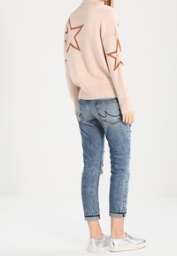 Ljusrosa stickad tröja med bruna stjärnor, parat med blå slitna jeans och silverfärgade slip-on skor. Mjuk textur och avslappnad passform.