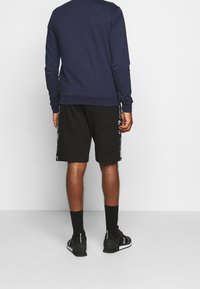 Marinsk blå sweatshirt och svarta shorts med vita sidostråk; textil med struktur, enkelt mönster, matchande svarta strumpor och träningsskor.