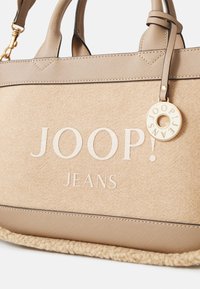 Beżowa torebka teksturowana z wytłoczonym logo "JOOP! JEANS". Strukturalna konstrukcja z lamówką ze splotu i dekoracyjną okrągłą zawieszką.