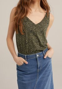 Haut sans manches vert olive avec un design imprimé léopard, présentant un décolleté en V et une coupe décontractée, associé à une jupe en denim bleu.