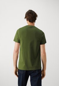 Camiseta de algodón verde oliva con manga corta y cuello redondo, con una textura suave y un ajuste relajado. Sin logotipos o patrones visibles.