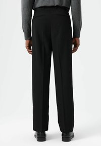 Pantalon noir taille haute à coupe large, avec une texture lisse et des poches arrière discrètes. Porté avec des chaussures noires.