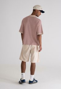 Short-sleeve, textured red and white patterned polo shirt, cream shorts, navy and cream sneakers, with a striped cap, viewed from the back.
