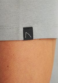 Pilka audinio apdaila su juodu žymekliu, ant kurio pavaizduotas minimalistinis baltas logotipas. Audinys lygus, o krašte matomi siūlai.