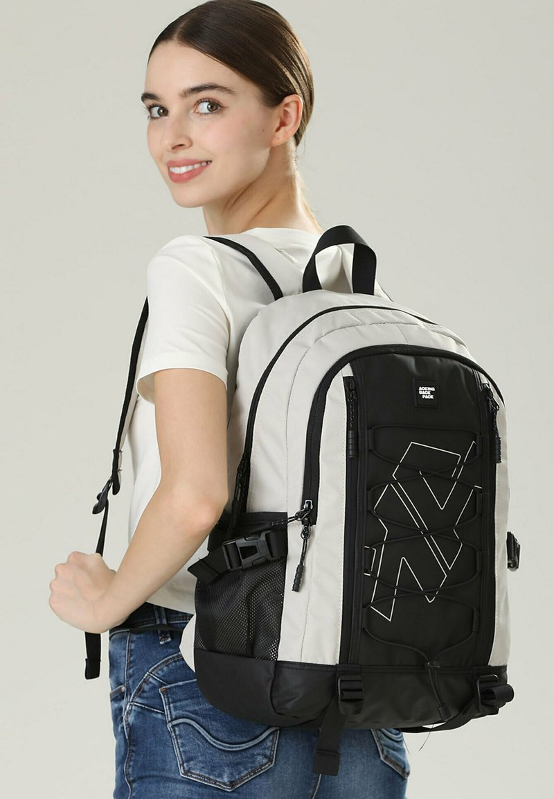 Zaino grigio e nero con un motivo geometrico, materiale resistente, spallacci imbottiti, tasche con zip e tasca laterale in rete.