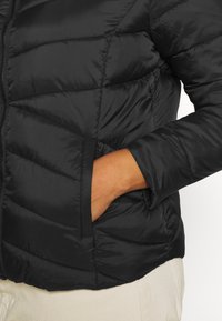 Schwarze Daunenjacke mit horizontalen Nähten, Reißverschluss und seitlichen Taschen. Das Material wirkt glatt und leicht.