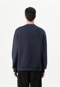 Sudadera de microfibra navy con un corte relajado, hombros caídos, puños y dobladillo acanalados, y un diseño de cuello redondo.