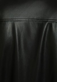 Tessuto in pelle nera con una texture liscia, caratterizzato da una leggera lucentezza e da un dettaglio a cucitura lungo la parte superiore, creando un design classico.