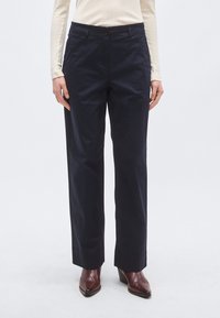 Pantaloni bleumarin cu croială dreaptă, închidere cu nasturi și textură subtilă. Asortați cu cizme maro cu toc pentru contrast.