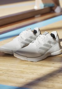 Scarpe sportive bianche con tomaia testurizzata, logo a tre strisce prominente e suola in gomma. Dotate di sistema di allacciatura e colletto imbottito.