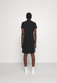 Svart polo klänning med korta ärmar, rak passform och kontrasterande sidosträck. Tillverkad av ett mjukt tyg, når till mitten av låren.