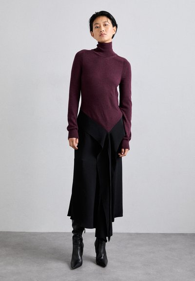 Burgunderfarget turtleneck-bluse med lange ærmer, parret med en sort lagdelt nederdel. Nederdelen har en spids kant og en flydende stofstruktur. Sorte ankelstøvler.
