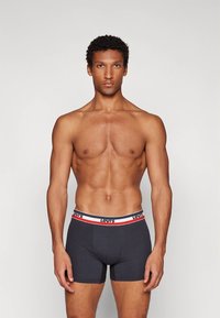 Cuecas boxer cinza escuro com um cós de marca apresentando detalhes em vermelho e azul. O material parece elástico e ajustado ao corpo.