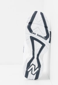 Bílá atletická podešev s texturovanou gumou, se vzorem cikcak a námořnicky modrými akcenty. Na boku je vytištěna značka „New Balance“.