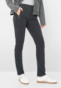 Pantaloni elasticizzati neri con vestibilità slim, dotati di una tasca laterale con zip e di una cintura elasticizzata. Abbinati a sneaker bianche.