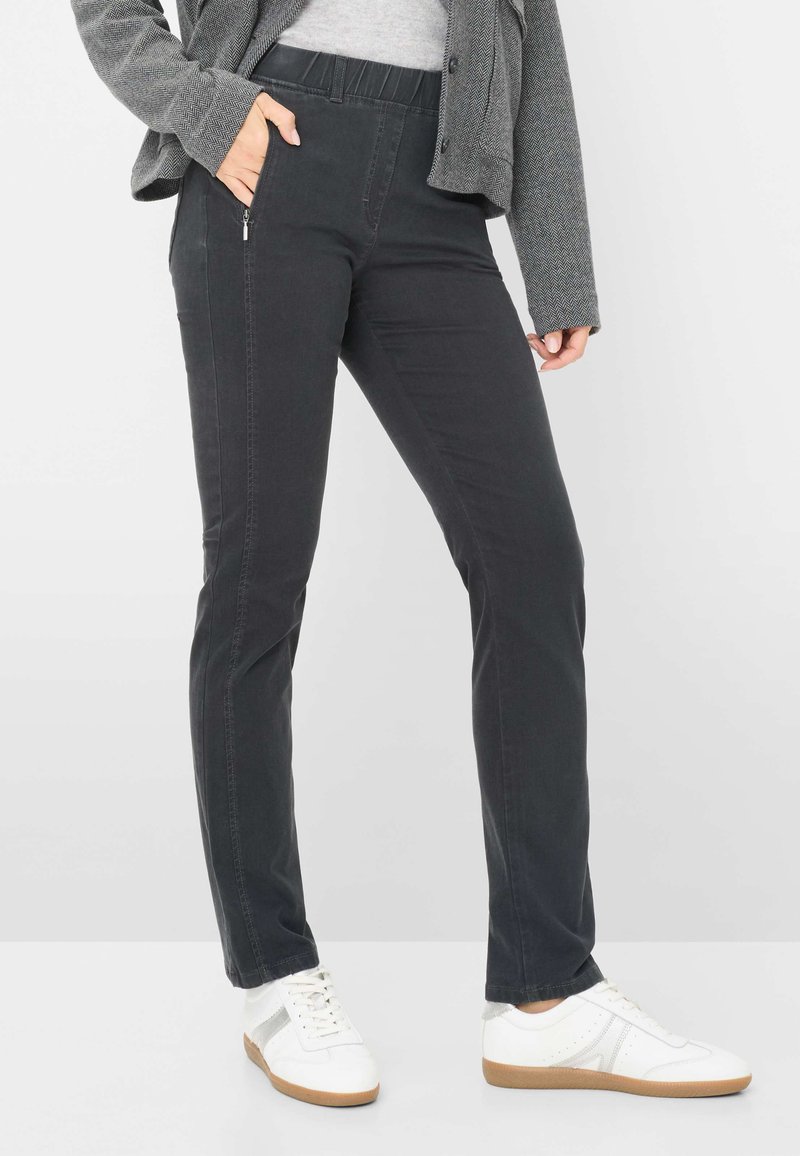Pantaloni elasticizzati neri con vestibilità slim, dotati di una tasca laterale con zip e di una cintura elasticizzata. Abbinati a sneaker bianche.