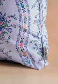 Jastučić s cvjetnim uzorkom u mekom, svijetloplavom materijalu. Ima ukrasnu ivicu s živopisnim ružama i lišćem. Oznaka glasi "Cath Kidston."