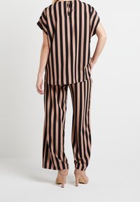 Top de rayas negro y nude con mangas cortas y detalle de abertura en la espalda, combinado con pantalones de rayas anchos a juego y tacones beige.
