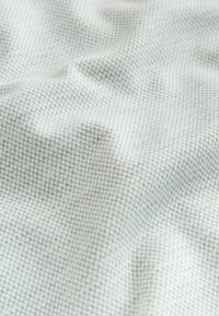 Vaaleanharmaa kangas, jossa on teksturoitu, ruudukkomainen kuvio; pehmeä pinta, jossa on vaihtelevia syvyyksiä ja hienovarainen kiilto.