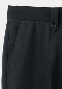Ceinture de pantalon noire avec poche latérale, passants de ceinture, patte de bouton et texture de tissu lisse visible en gros plan.