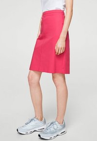 Jupe rose mi-longue au design ajusté, fabriquée dans un tissu lisse. Assortie à des chaussures de sport bleu clair. Poches latérales visibles.