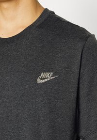 Close-up of a black crewneck t-shirt with a small, multicolored glittery Nike logo on the chest.