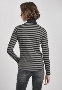 Langærmet bluse med sorte og grå striber, der har høj hals og blødt materiale. Kombinationen med tætsiddende mørke jeans.